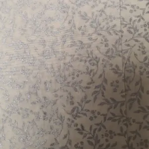 Beige Stoff mit silbernen floralen Mustern und feinen Details auf der Oberfläche.